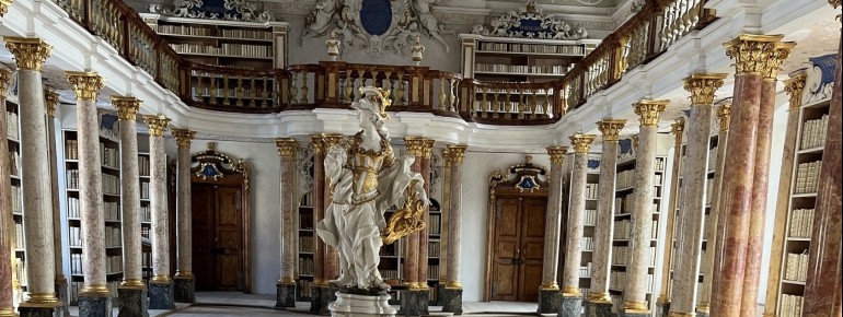 Der prachtvolle Bibliothekssaal beeindruckt mit kunstvoll verzierten Regalen und einer Sammlung jahrhundertealter Bücher.