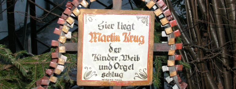 Das Grabkreuz mit der Inschrift „Hier liegt Martin Krug, der Kind, Weib und Orgel schlug“ stammt aus der Tiroler Ortschaft Wiesing.
