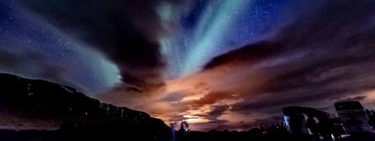 Nordlichter in Westisland am 12. April 2018. Der orange Farbbereich entspringt den Lichtquellen der etwa eine Autostunde entfernten Stadt Reykjavík.