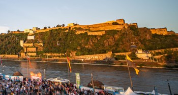 During the Koblenz Summer Festival, visitors celebrate at the Deutsches Eck, while Ehrenbreitstein Fortress glows in the golden evening light.