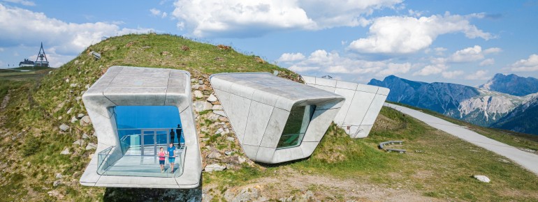 Three large window fronts break through the mountainside, framing targeted panoramas of the Dolomites, the Ortler and the Zillertal Alps.