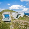 Three large window fronts break through the mountainside, framing targeted panoramas of the Dolomites, the Ortler and the Zillertal Alps.