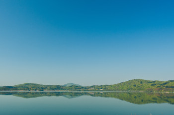 Im See spiegeln sich die umliegenden Hügel und Berge der Eifel.