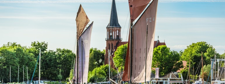 Wustrower Zeesbootregatta: Historische Segelboote mit rotbraunen Segeln gleiten über den Bodden – ein maritimes Traditionsevent im Sommer.